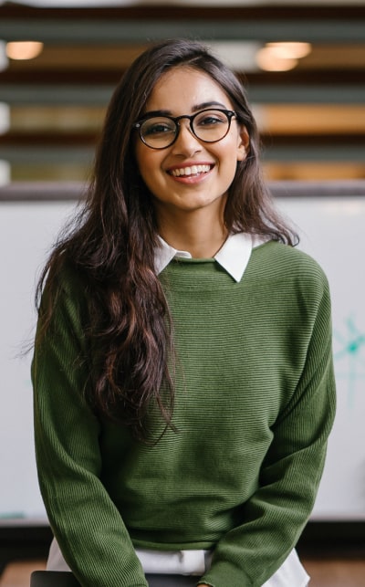 Smiling woman in green sweater with glasses.
